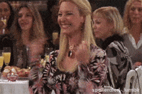 Friends gif. At a banquet, Lisa Kudrow as Phoebe Buffay points to herself excitedly and laughs.