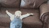 Video gif. A toddler is passed out half on and half off a couch. Their arms are splayed fully outwards and they look sloshed.