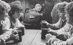Movie gif. In black and white, Elijah Wood as Frodo, Sean Astin as Samwise, Billy Boyd as Pippin, and Dominic Monaghan as Merry in Lord of the Rings lift up mugs of ale in a toast.