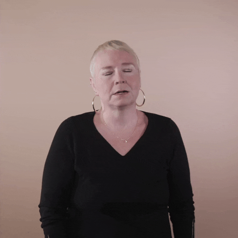 Reaction gif. A white woman with invisible disabilities, with hair styled in a sleek platinum pixie cut and big hoop earrings drops her head back, eyes closed, then looks at us with exasperation in her eyes and says, "Tired."