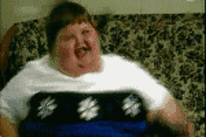 Video gif. An overweight child smiles and bounces happily on a couch.