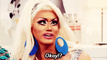 Video gif. Drag queen crosses her eyes inward and turns towards a person to sassily say, “Okay!?”