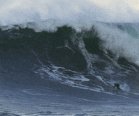 Video gif. A lone surfer rides a massive wave as it crashes down toward him.