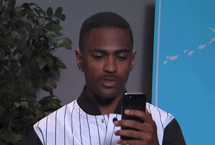 Celebrity gif. Big Sean reads on his phone, then looks at us with a straight face.