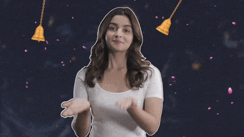 Celebrity gif. Bollywood actor Alia Bhatt, cartoon bells and rose petals around her, draws circles with her hands, palms facing up, in a gesture of spiritual offering, then paints a tilaka between your eyes.