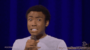 Celebrity gif. Donald Glover looks at the camera with a still grimacing expression. He tugs on the collar of his shirt and winces.