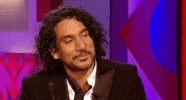 Celebrity gif. Naveen Andrews is leaning back and considers a question before opening his mouth to speak.