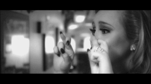 Celebrity gif. Black and white shot of Adele lifting up her hands to show her crossed fingers while she smiles hopefully.