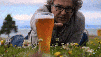Video gif. Man lies in a meadow, desperately reaching for a glass of beer before it suddenly disappears, leaving him devastated.