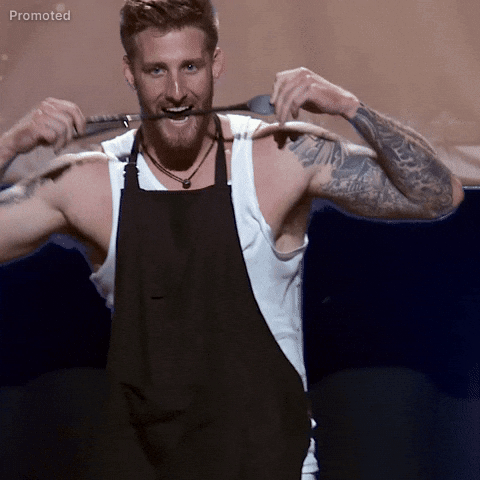 Sponsored gif. Sam McKinney, a contestant from season 21 of The Bachelorette, puts a cooking spatula in his mouth and smiles as he walks towards us with seductive confidence and claps his hands together in front of him.