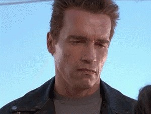 Movie gif. Arnold Schwarzenegger as The Terminator learning to smile. He stares blankly before turning up the corners of his mouth in a very stiff smile. He tries again and almost accomplishes it before dropping his smile and defaulting into his blank, serious look.