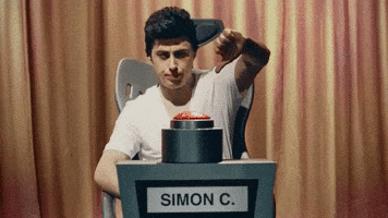 Video gif. Man sits in a game show chair with a big red button and a sign that says, “Simon C.” in front of him. He frowns, shaking his head, and gives a big thumbs down.