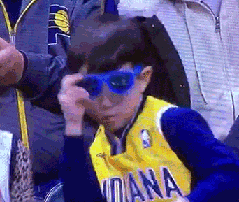 Video gif. A little boy in a basketball jersey pulls off his shades while dancing in the stands. He confidently points at us.