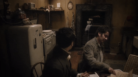 Movie gif. Taika Waititi as Viago and Jonny Brugh as Deacon sit at a kitchen table, one looking at a piece of paper, the other putting his head in his hands defeatedly.