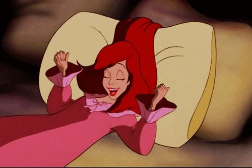 Disney gif. In human form, Ariel from the Little Mermaid stretches out in bed and rolls onto her side, nuzzling into a fluffy pillow.