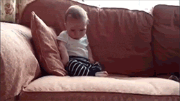 Video gif. A sleeping baby sits upright on a couch and suddenly, in one swift motion, tips over and falls face first into the cushion. 