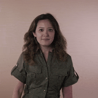 Reaction gif. A Disabled Vietnamese-American woman hemorrhagic stroke survivor with left-sided hemiplegia, brown sun-bleached hair styled in waves facepalms with a cringe.