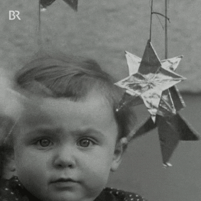 Holiday gif. Wide-eyed baby swipes at Christmas star cutouts dangling in front of him.