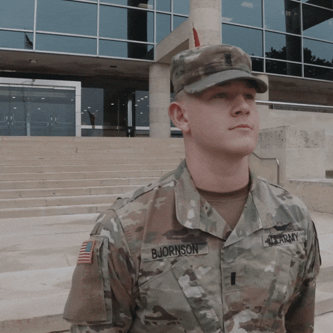 Video gif. Private B Jornson, dressed in US Army fatigues, standing at attention, brings his hand to the brim of his hat, marking a salute.