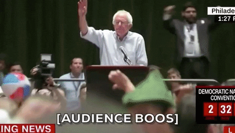 Political gif. In a clip from the news, we zoom out on Bernie Sanders at a podium to see a large audience. Some of the people are making thumbs-down gestures. Text: "Audience boos."
