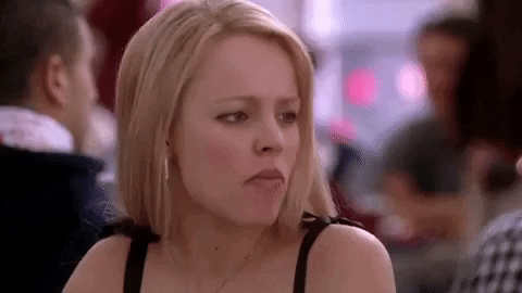 Movie gif. Rachel McAdams as Regina George in Mean Girls frowns and gives a quizzical look at someone while chewing.