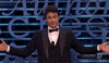 Celebrity gif. James Franco stands in front of a podium with outstretched arms and a boastful, closed mouth smile, looking up and down at the audience.