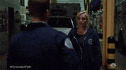 Tv gif. Kara Killmer as Sylvie Brett on Chicago Fire stands in front of a fire hall with an ambulance parked in the garage and Jesse Spencer as Matthew Casey runs up to her, caresses her neck, and they passionately kiss each other.