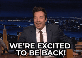 Tonight Show gif. An enthusiastic Jimmy Fallon slaps both hands on his desk, saying, “We're excited to be back!”
