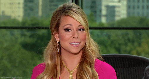 Celebrity gif. Mariah Carey smiles awkwardly while her eyes search around in confusion.