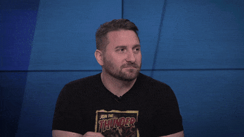 TV gif. John Iadorola on The Young Turks looks at someone offscreen and gives them the middle finger with an amused smirk. 