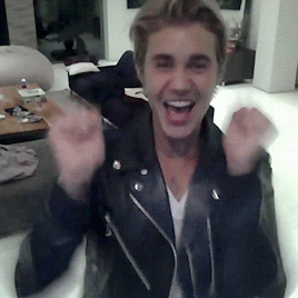 Celebrity gif. Justin Bieber does a happy jig in his home by pumping his arms into the air and crossing them in and out while slowly backing away from us.