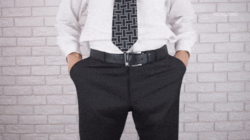 Video gif. Shot of a man's hips and legs who is wearing trousers and a belt. He pulls out his pockets to show us that they're completely empty.