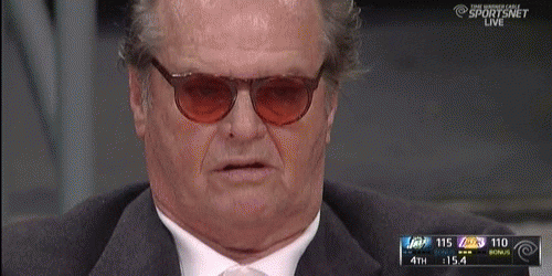 Celebrity gif. Jack Nicholson sits in the audience of a sports game. He wears tinted sunglasses and looks at the game with darting eyes. His mouth is slightly open as if bored.