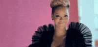 Celebrity gif. Rihanna, wearing a billow-sleeved black dress, smiles and covers her face with her hands like she's slightly embarrassed.