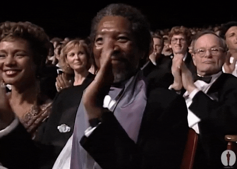 Celebrity gif. Morgan Freeman sits amongst a crowd at an award show. He looks up at the stage with admiration and a wide smile spread across his face. He gives big, strong claps to signify how proud he is. 