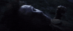 Movie gif. Thomas Kretschmann as Dr. Andre Mason in Discarnate lies on his back in the dark as his head wobbles and he looks disoriented.