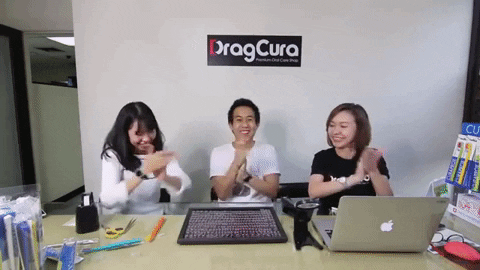 Video gif. A man and two women sit behind a desk clapping their hands and smiling.