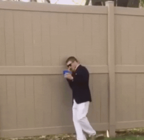Video gif. A shaky camera takes footage of a man in a blazer and sunglasses as he speaks into a phone. He appears to be drunk: he's carrying a plastic blue cup in one hand as he stumbles backwards, and when he falls over, he spills its contents.