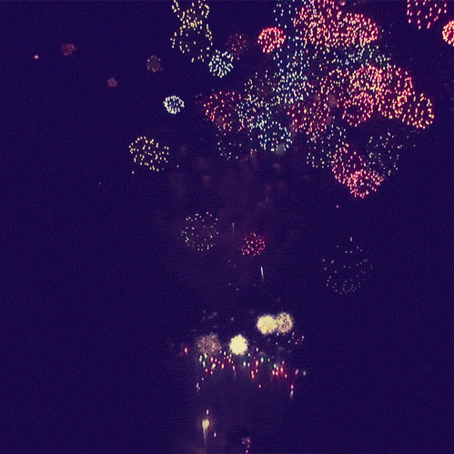 Video gif. Countless fireworks explode over a dark background. They blaze from the bottom and burst into circles of red, yellow and blue. 