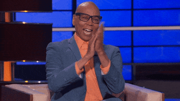 Reality TV gif. RuPaul cheers and claps enthusiastically, seated on a couch on the set of To Tell the Truth.