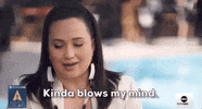 Oscars 2024 gif. Lily Gladstone, wearing a white blazer and white dangly earrings, glances down and says, "Kinda blows my mind," which appears as white text on the bottom. 