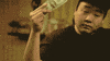 Video gif. David Cho, a Youtuber, is doing a shoulder dance and looks swaggy. He holds a one dollar bill in one hand and makes it rain, with one single dollar bill.