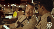Movie gif. In a restaurant, Kevin Heffernan as Mac in Super Troopers leans over and smiles as he playfully pokes Thorny, played by Jay Chandrasekhar.