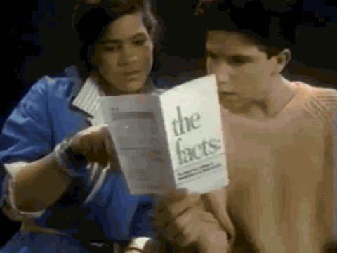 Video gif. 80s video of two teenagers sit side by side. A boy holds up a paper pamphlet in front of them as a girl runs a finger down its page. The title of the pamphlet clearly reads, "the facts."