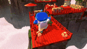 Video game gif. A clip of gameplay from the trailer for Playstation video game "Astro Bot" shows a supersized Astrobot running across a red Chinese-inspired wooden platform filled with obstacles like boxes and bamboo railings. As Astrobot collides with the obstacles, they explode, sending green balls and particles flying across the stage. The stage is set on a mountaintop, with several Chinese-inspired red pathways leading to a temple in the background. 