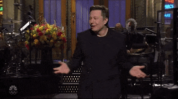 SNL gif. Elon Musk is on SNL and he looks awkward as he moves back and forth with his arms out and a goofy smile on his face.
