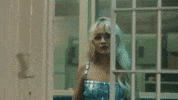 Music video gif from Sabrina Carpenter's music video for "Please Please Please." She wears a silver tank top and stands outside of a jail cell looking forlon as the door to the cell slowly closes.