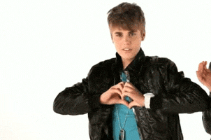 Celebrity gif. Young Justin Bieber makes a heart with his hands over his chest, then wiggles his fingers as his shoulders pull back.