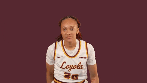 Sports gif. Destiny Jackson from the Loyola Ramblers women's basketball player looks at us with a faux shocked expression as she raises one hand in a rock on symbol, then the other, then waves both hands in circles at us. 