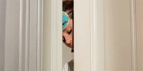 Movie gif. Audrey Hepburn as Holly in Breakfast at Tiffany's wears an eye mask as she pokes her head out a door with sleepy eyes closed.